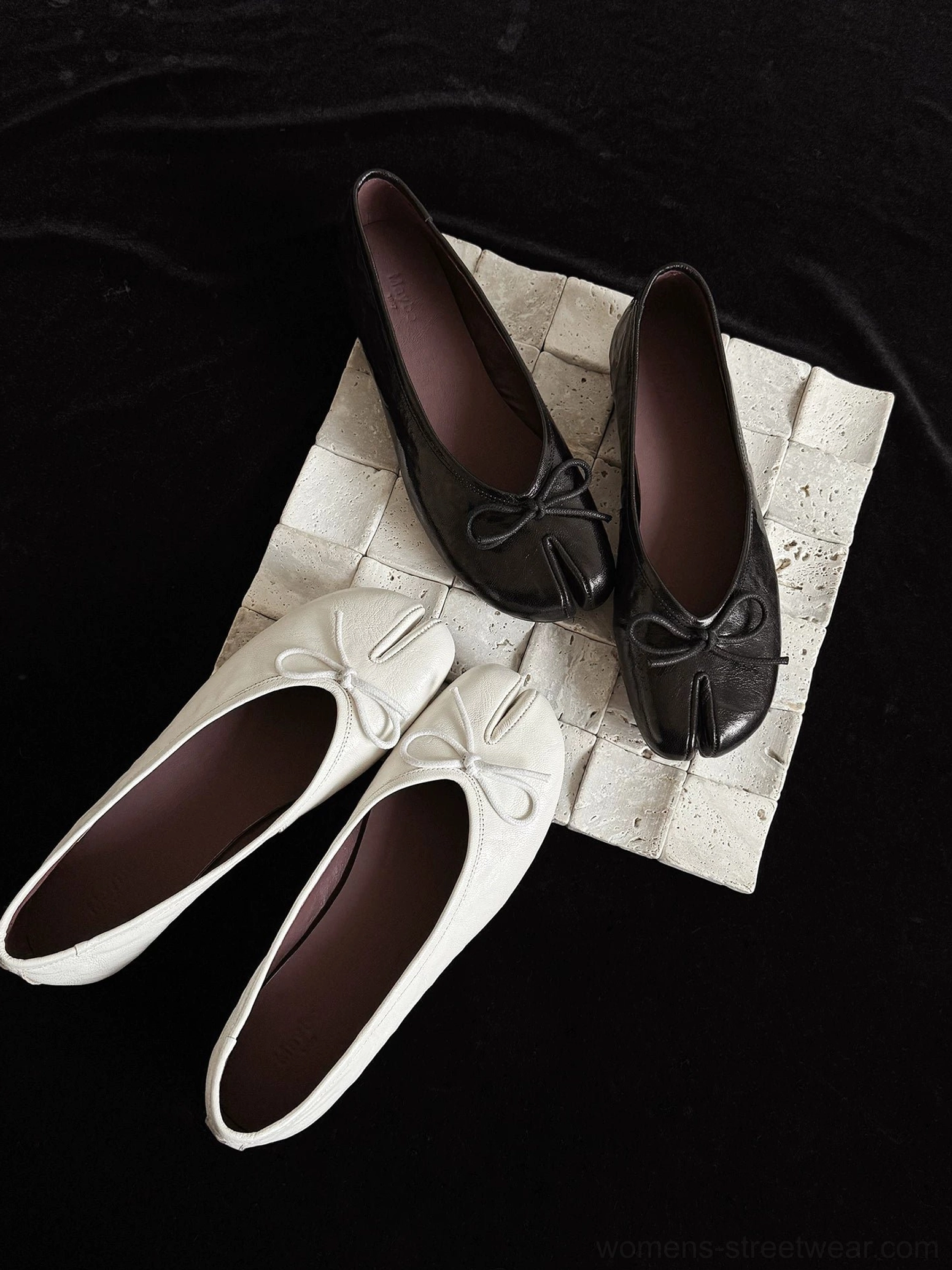 Black and ivory split-toe leather ballet flats with front bow detail displayed in flat lay product view