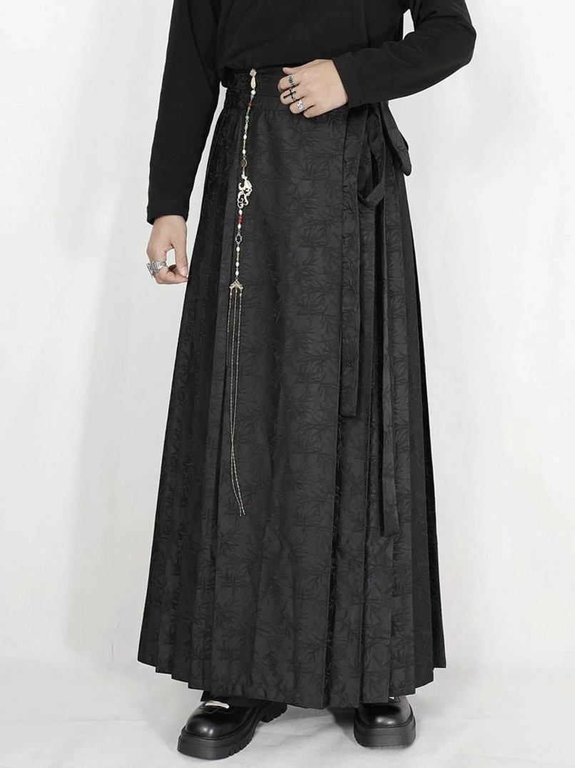 Low angle view of black jacquard pleated maxi skirt featuring side sash tie tassel chain and chunky black shoes