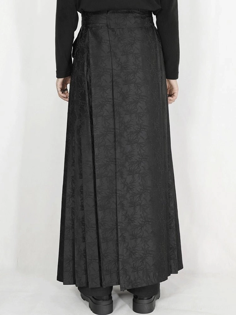 Black pleated maxi skirt in textured jacquard fabric featuring side tie sash and hanging tassel chain