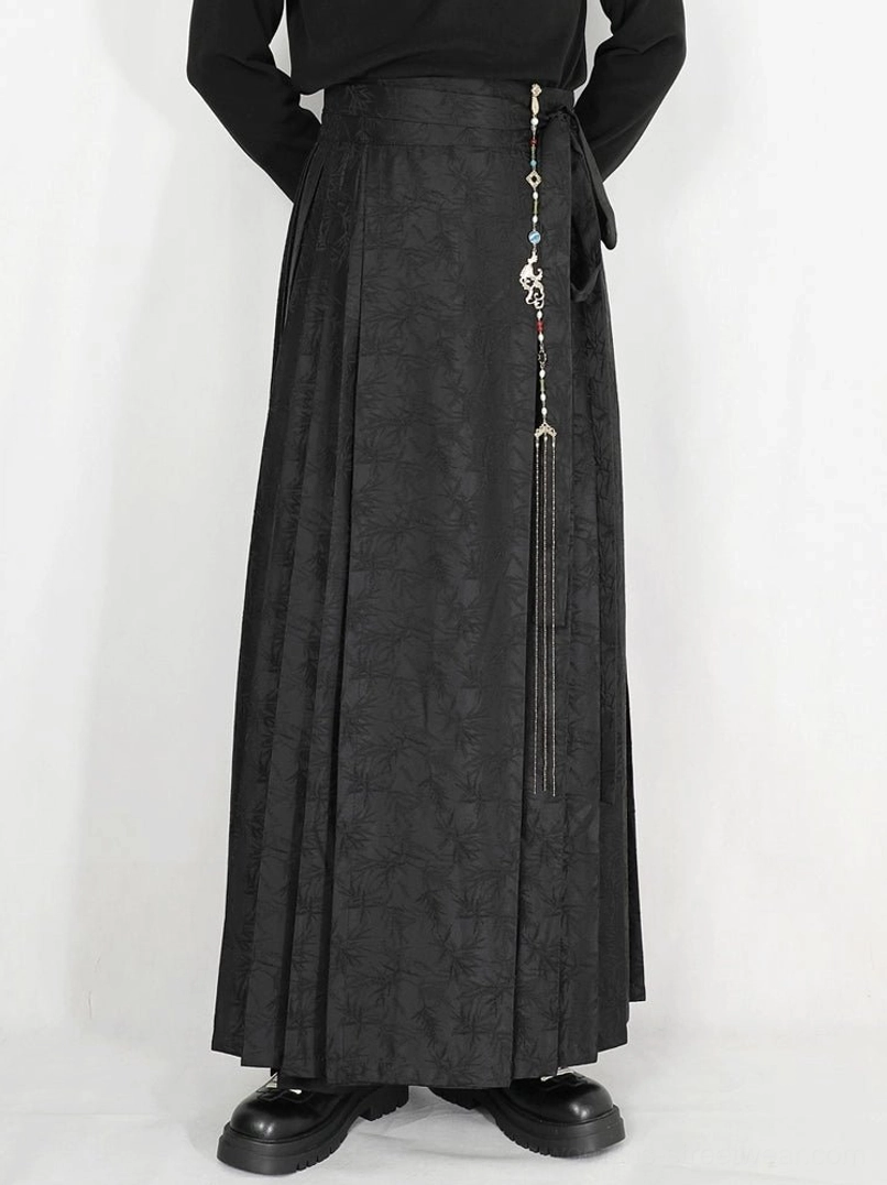 Close-up of black jacquard pleated maxi skirt wrap waist with side tie sash and decorative tassel chain