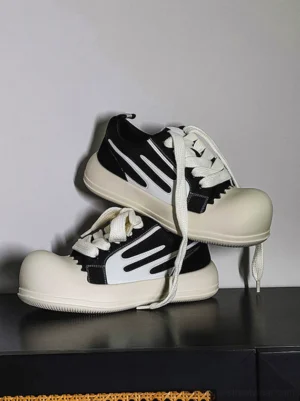 Black chunky platform sneakers with white oversized toe caps, curved white side panels, white laces and thick jagged-edge streetwear sole