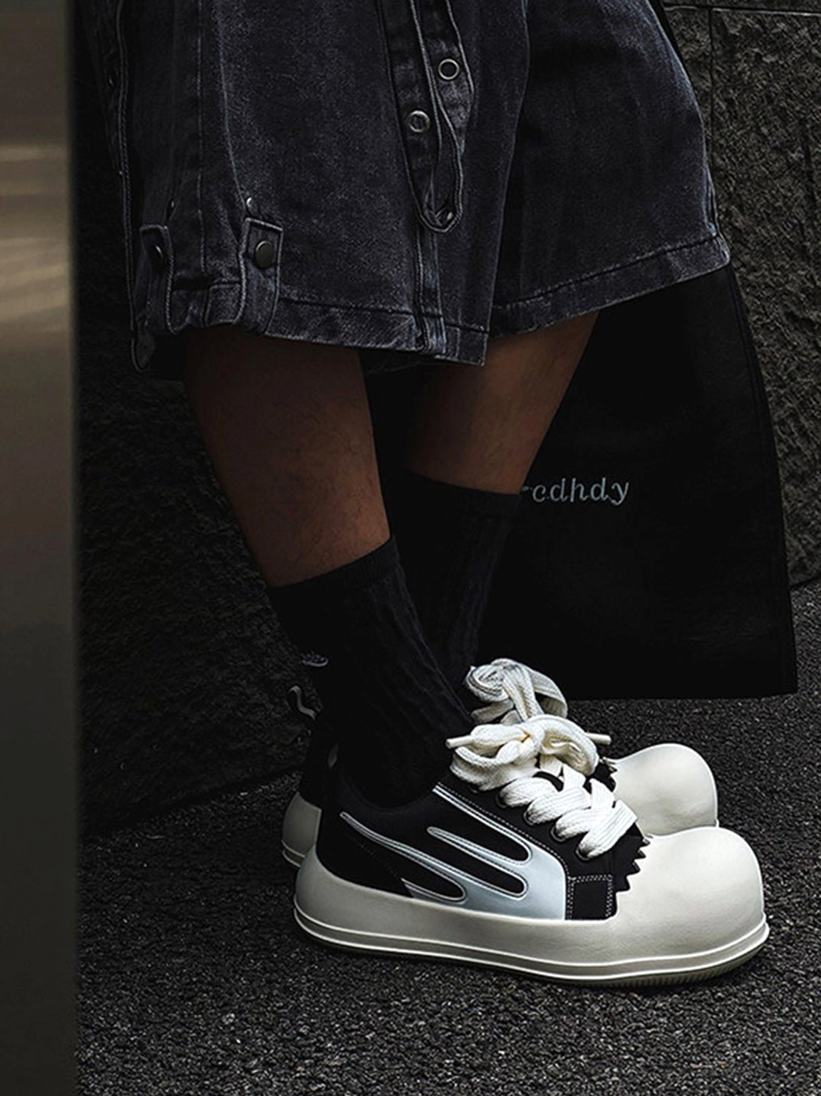 Black chunky platform sneakers with silver white side accents and oversized white toe caps worn with dark denim shorts outdoors