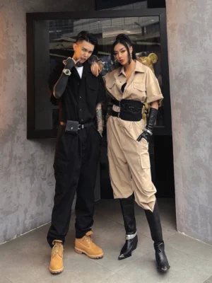 Black and khaki utility cargo jumpsuit outfits with wide belts and work boots against a concrete studio wall