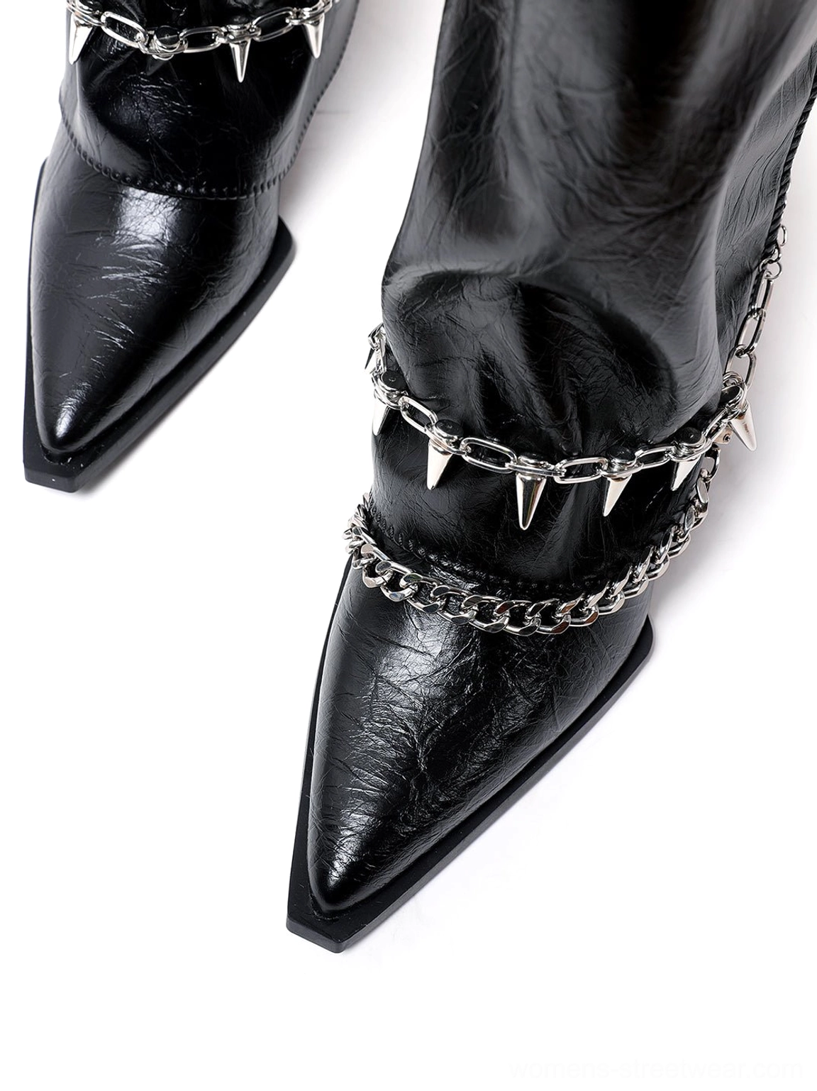 Detailed view of black knee-high chain riding boots featuring a pointed toe, crinkled finish, metal buttons, and punk-inspired ankle hardware
