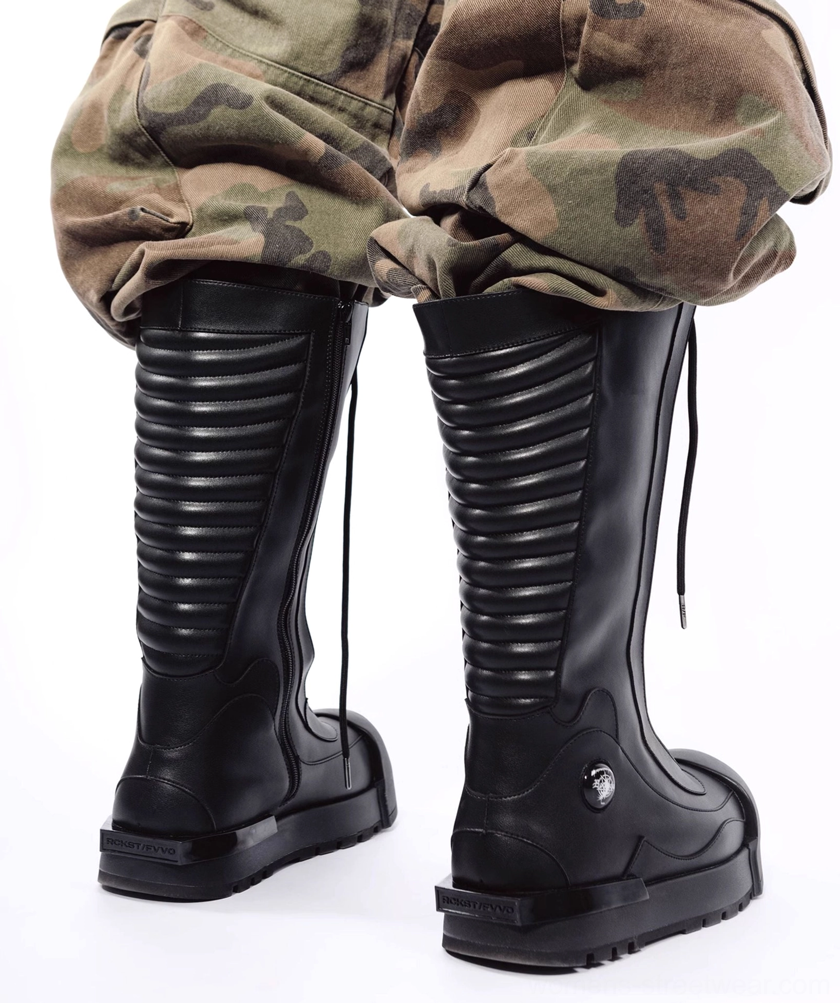 Model wearing black knee-high platform combat boots with camo cargo shorts, showing the rear lacing details and industrial streetwear styling