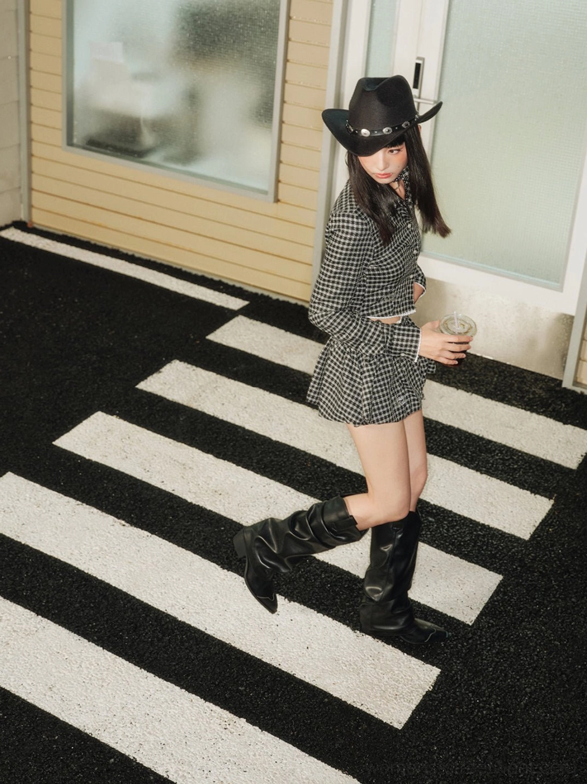 Black leather-look knee-high Western boots styled with a houndstooth set and cowboy hat in a modern streetwear outfit