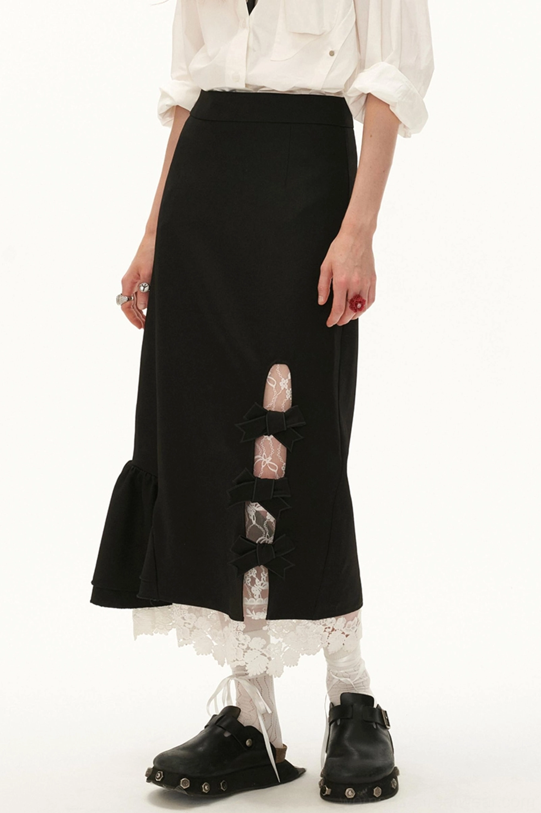 Black lace bow side-slit ruffle hem midi skirt styled with a white blouse, lace socks, and black platform loafers in a front side view
