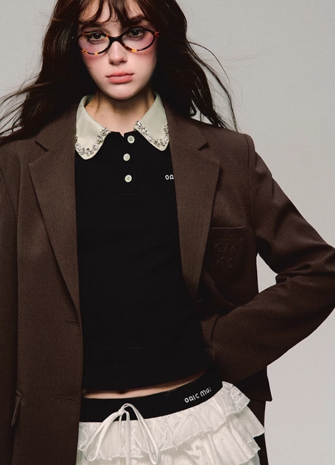 Close front view of black lace collar cropped polo top showing puff sleeves button placket and chest letter embroidery