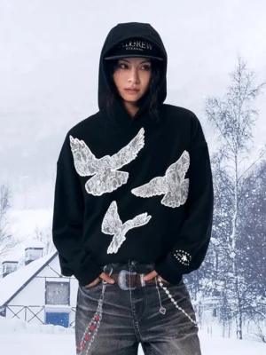 Front full-body view of a black lace dove statement hoodie styled with vintage jeans and chain accessories in a snowy winter streetwear setting