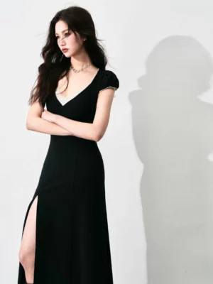 Black lace-trimmed thigh-slit column maxi dress shown from the left three-quarter view with fitted silhouette, white lace V-neck, and cap sleeves