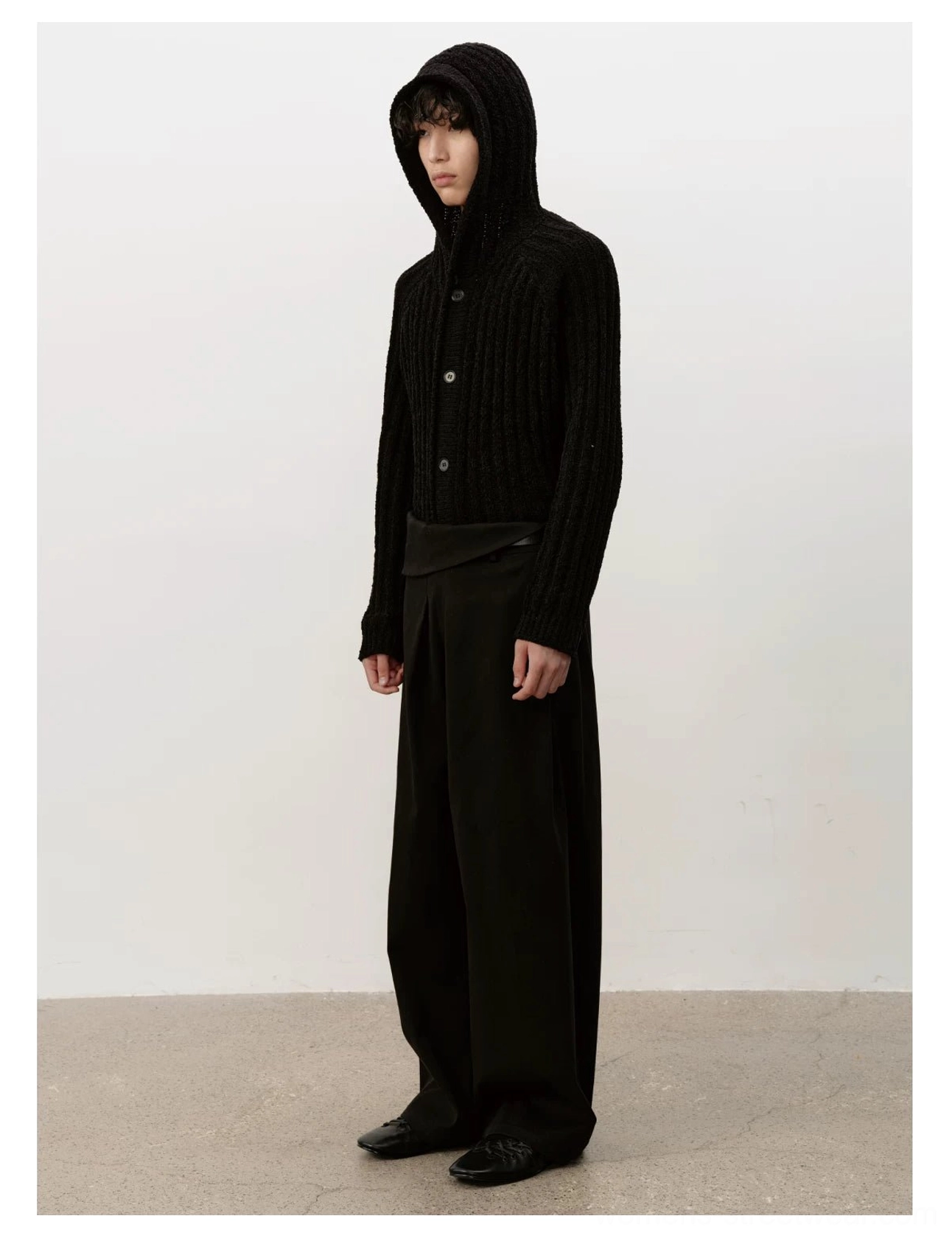Black lace-up ballet sneakers styled with a hooded knit cardigan and wide-leg trousers in a tonal avant-garde streetwear look