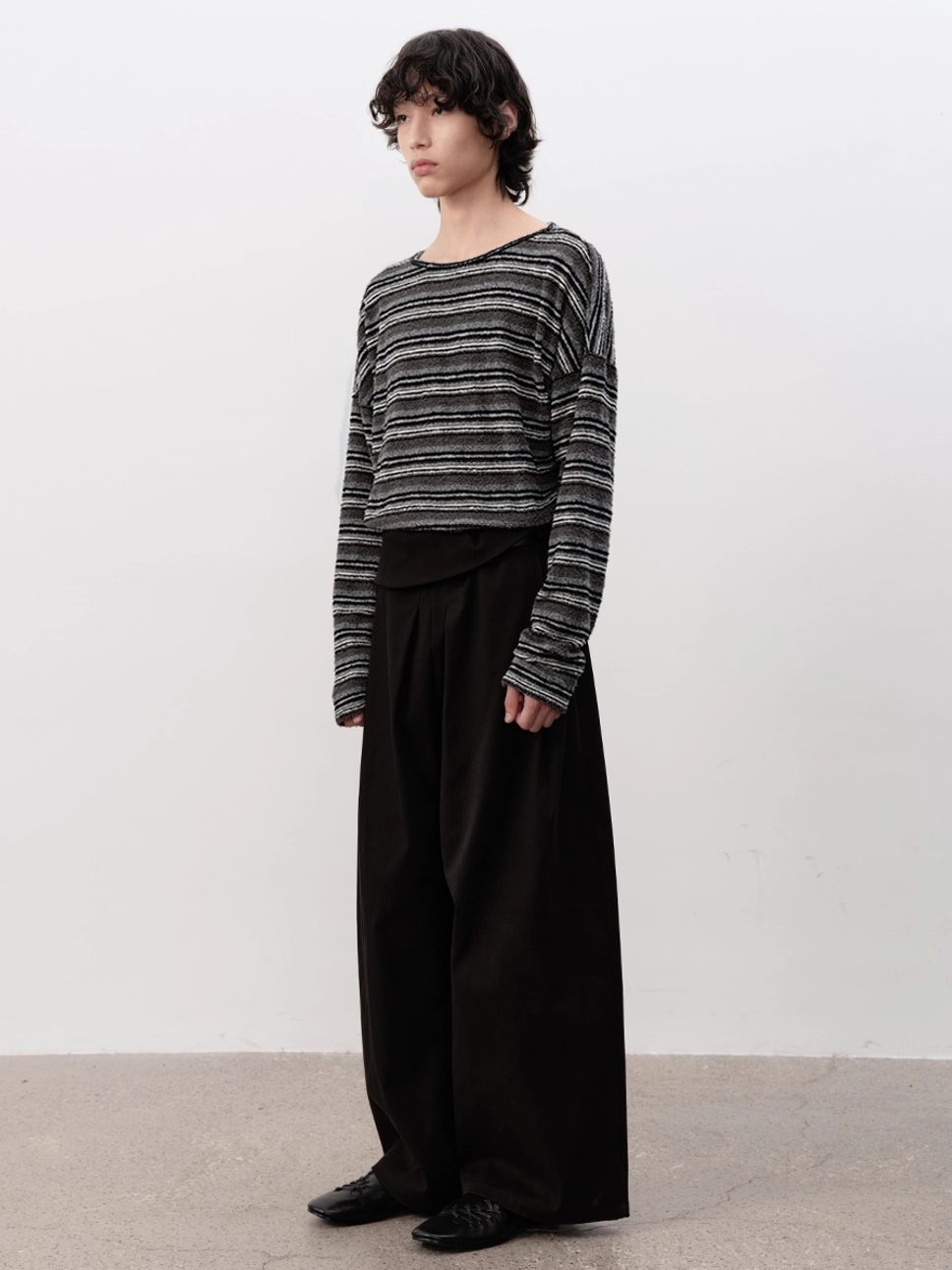 Side view of black lace-up ballet sneakers styled beneath wide-leg black trousers in a minimalist Korean streetwear outfit