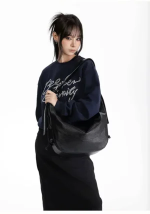 Black lace-up crescent hobo shoulder bag styled with a navy graphic sweatshirt and black midi skirt in Korean streetwear outfit