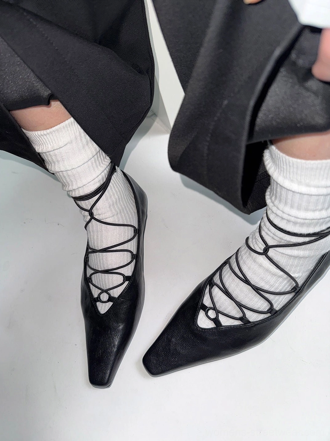 Black lace-up Mary Jane flats styled with white crew socks and wide-leg black pants, highlighting the sleek crossed lace design