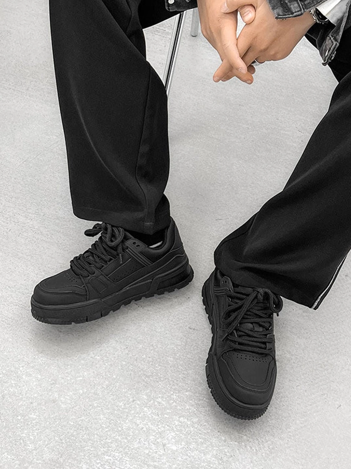 Black lace-up platform sneakers worn with a dark denim jacket and wide-leg trousers highlighting the matte upper and substantial sole
