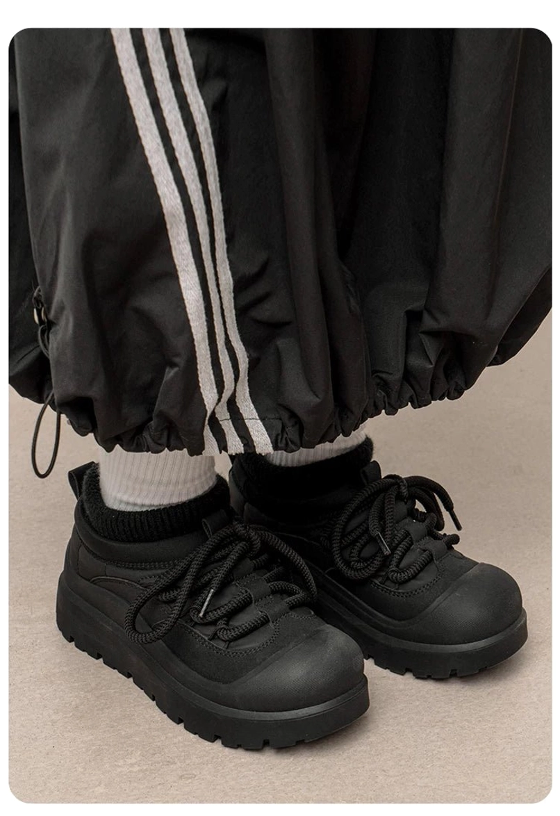 Low front-angle view of black lace-up platform sneakers worn with striped track pants and white socks