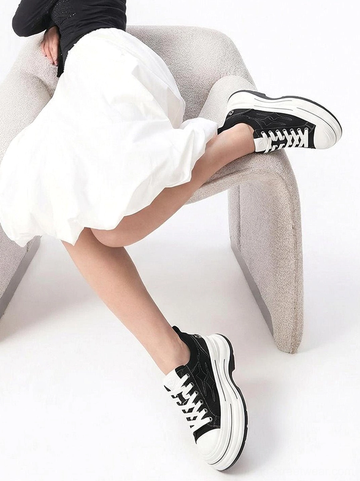 Female model wearing black layered platform canvas sneakers with white sole, black top, and white ruffled skirt in a Seoul-inspired streetwear outfit