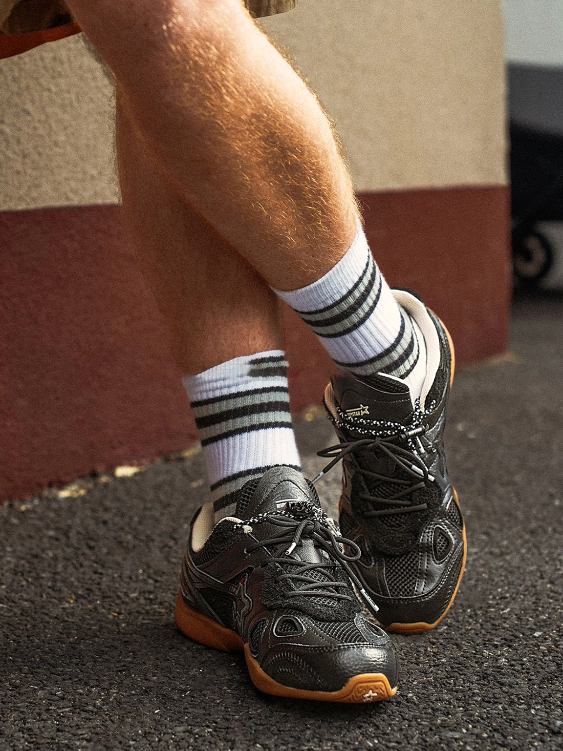 Close-up of black layered running sneakers worn with striped crew socks on asphalt, showing the retro streetwear styling