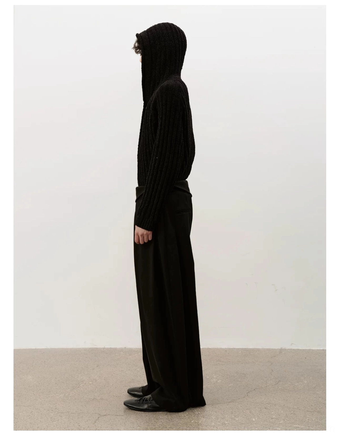 Side view of low-profile black leather ballet sneakers with hooded knit cardigan and relaxed wide-leg trousers
