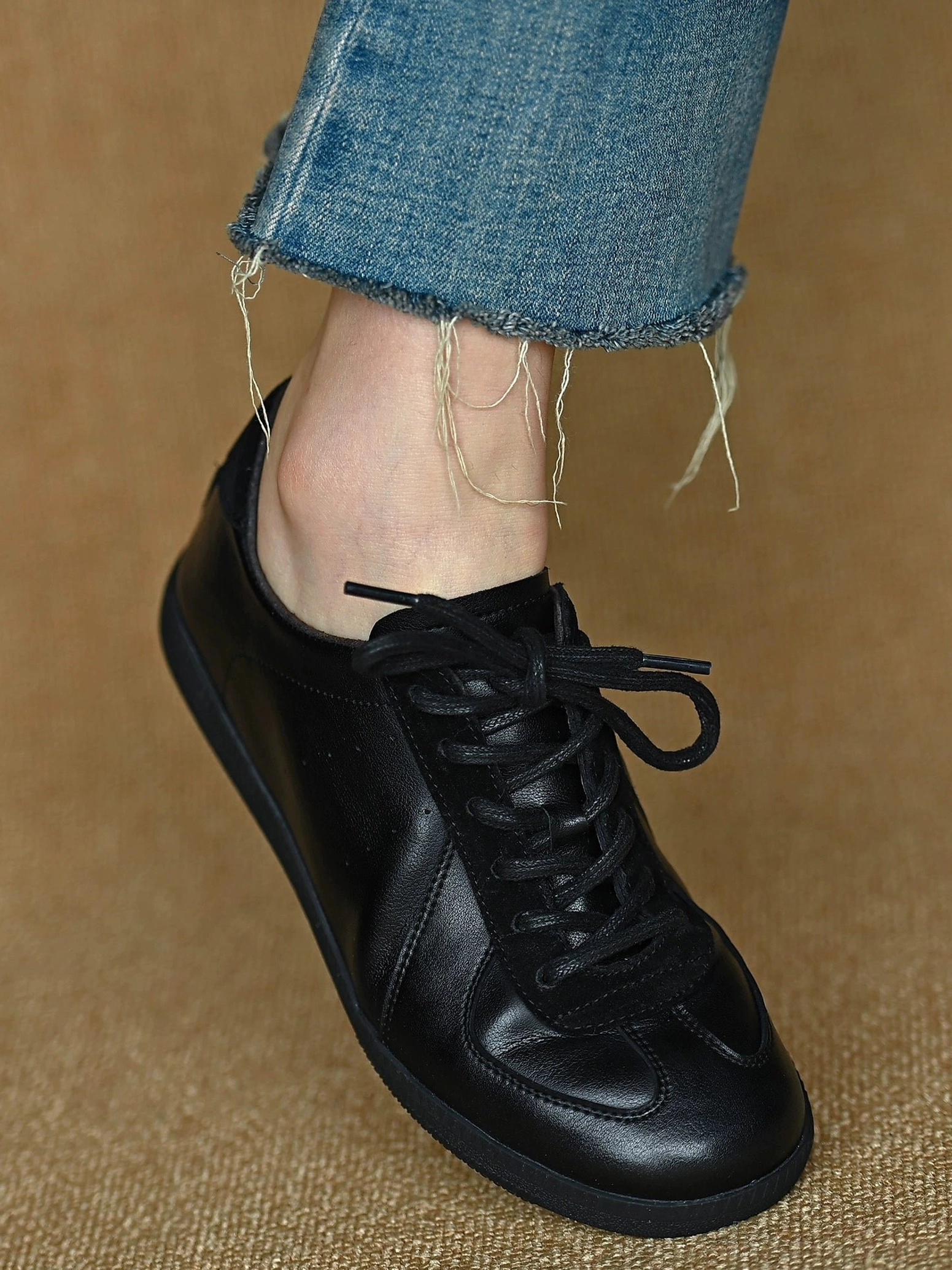 Black leather German trainer-inspired low-top sneakers worn with frayed cropped blue jeans in a minimalist streetwear outfit