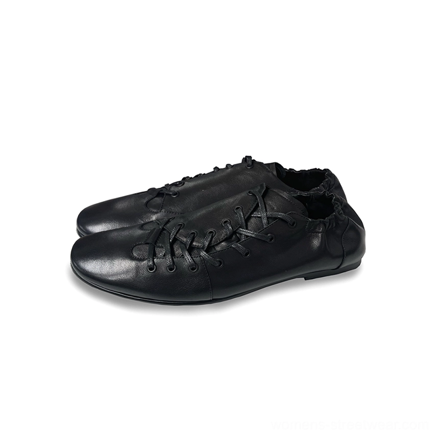 Overhead flat lay of black leather lace-up ballet sneakers featuring crisscross waxed laces, soft rounded toe, matte upper, and thin rubber sole