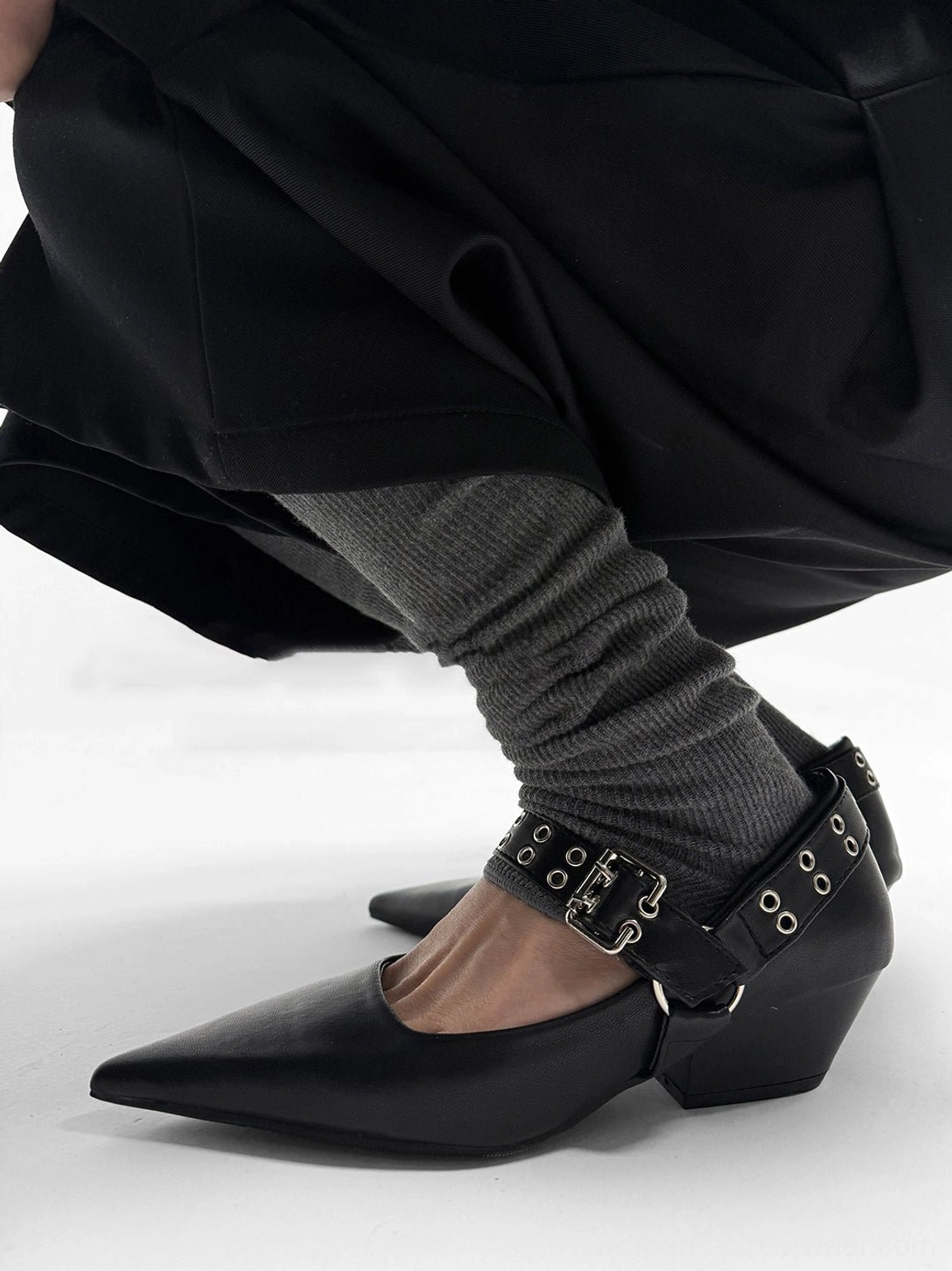 Black leather-look pointed Mary Jane pump with low block heel and grommet detailed ankle strap worn with dark clothing