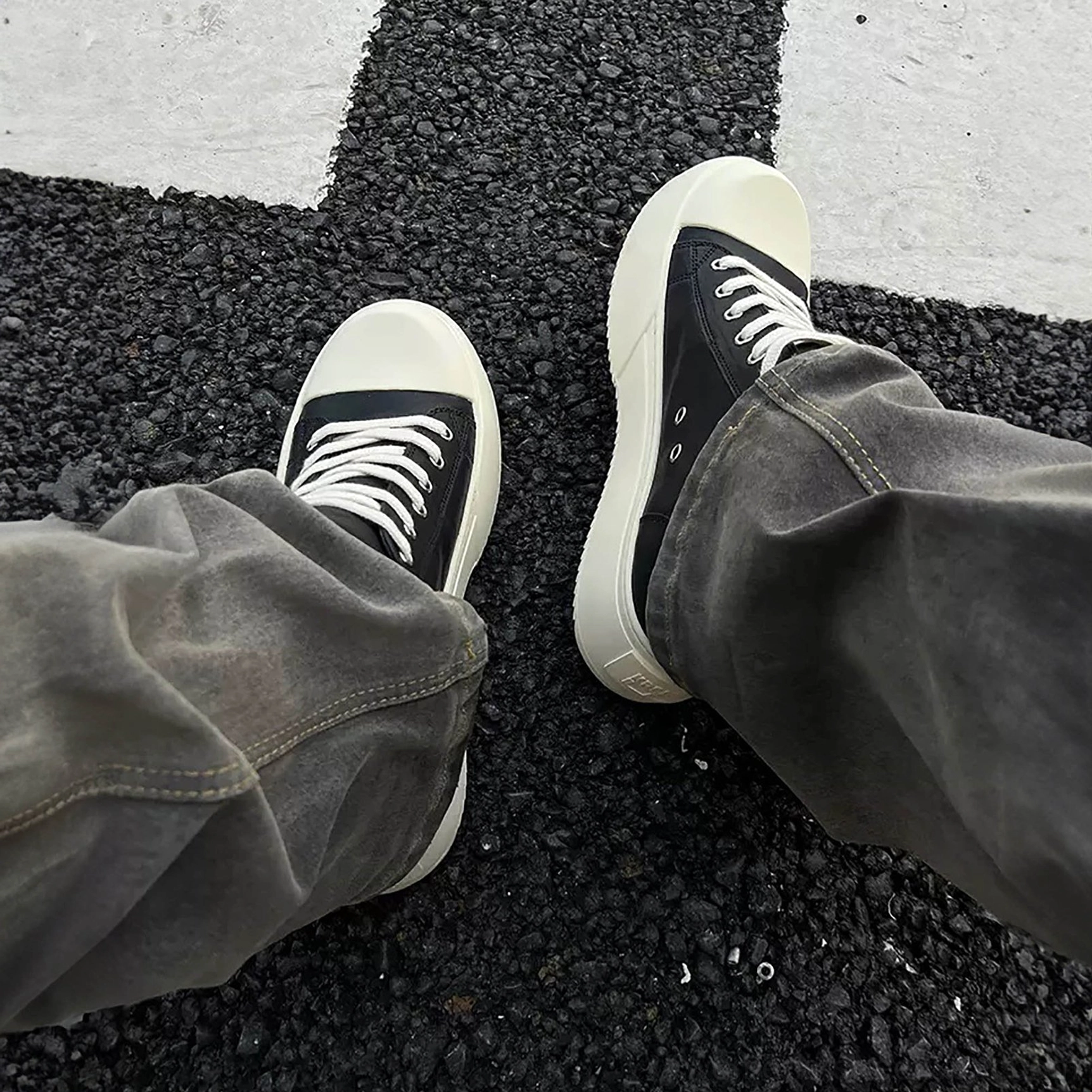 Top-down view of black leather low-top platform sneakers with off-white soles worn with relaxed gray jeans