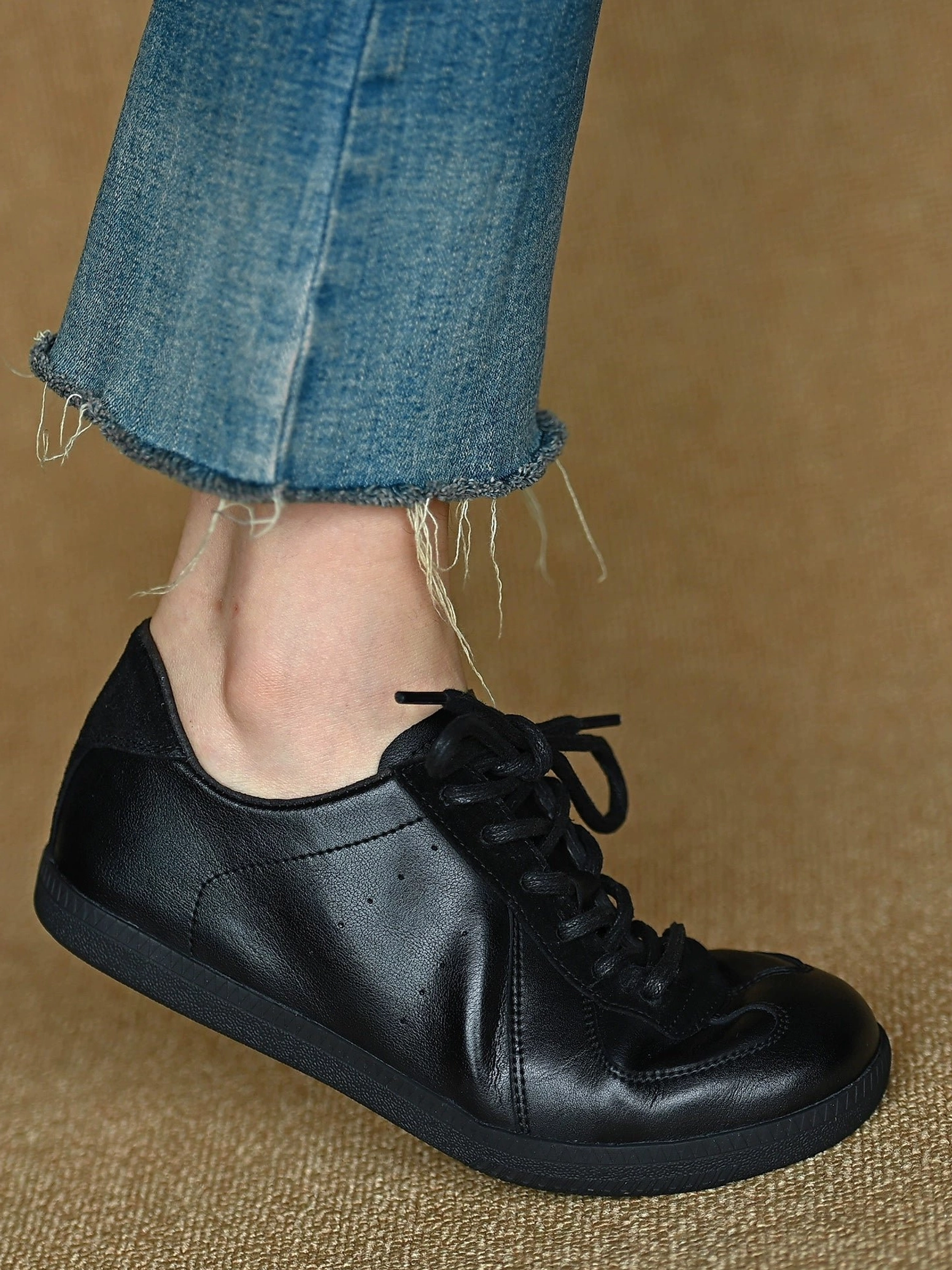 Rear side view of black leather low-top sneakers worn with cropped blue denim and casual urban streetwear styling