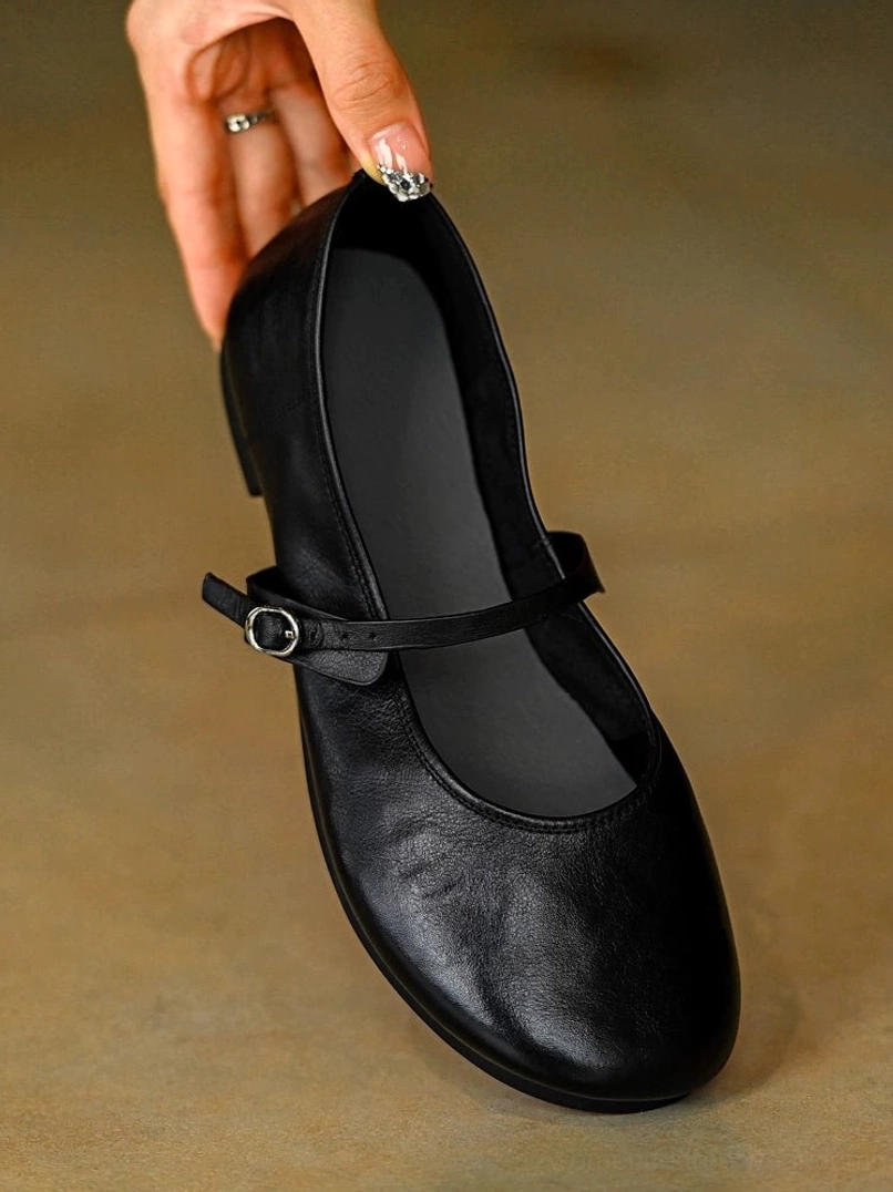 Black leather Mary Jane flat shoe shown from the front side with smooth leather upper rounded toe and adjustable buckle strap