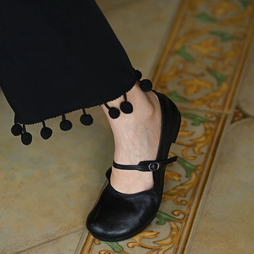 Side close-up of a black leather Mary Jane flat worn with cropped trousers showing adjustable strap and low profile sole