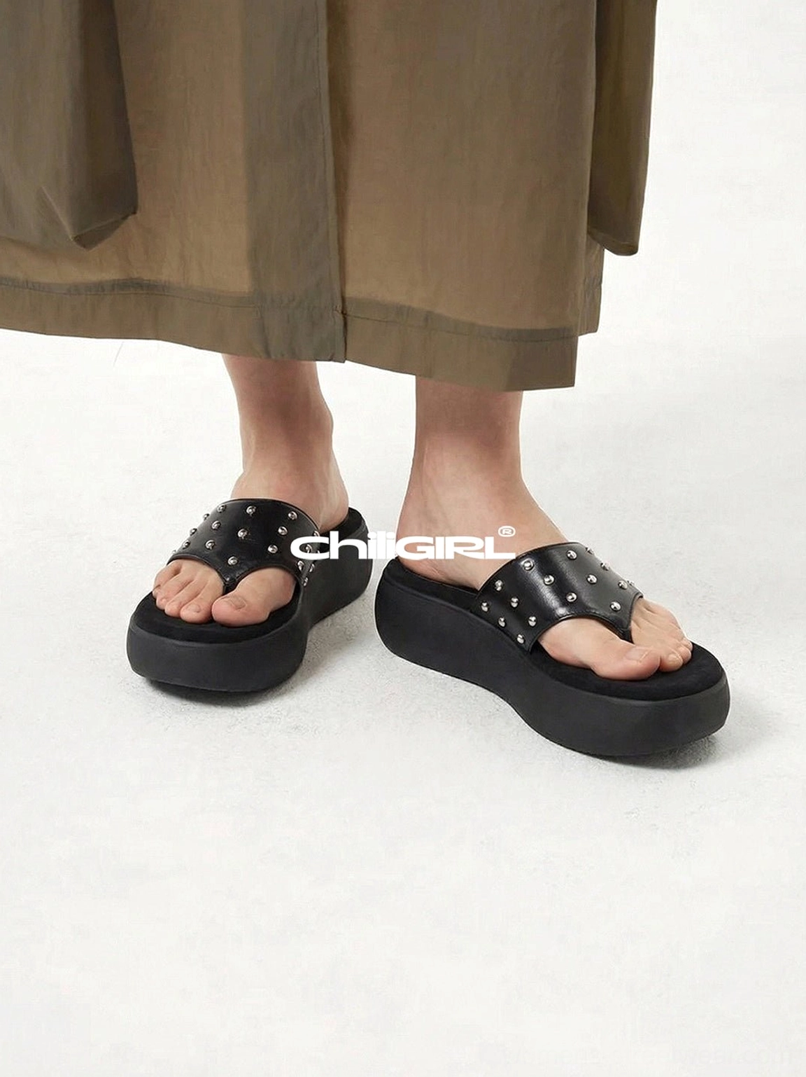 Front view of black leather platform thong sandals styled with a brown midi skirt
