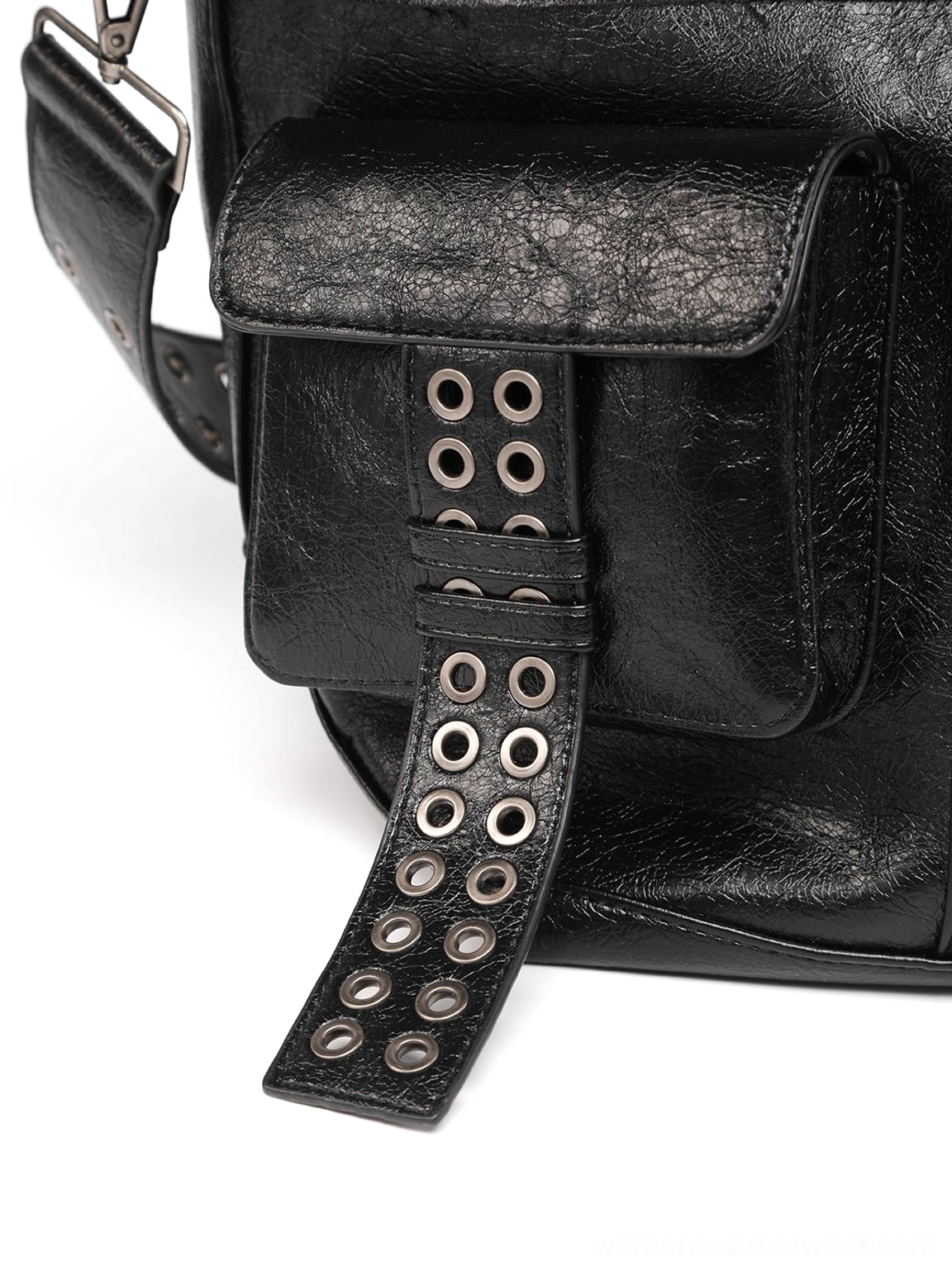 Close-up of black leather tote bag outer utility pocket with flap construction and eyelet-studded decorative strap detail