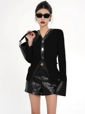 Front view of a black leather-trimmed textured knit cardigan jacket styled with patent shorts knee-high boots sunglasses and a handbag