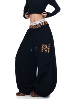 Black leopard trim wide-leg fleece sweatpants shown from the front three-quarter view with oversized baggy fit drawstring waist and leopard patch pocket