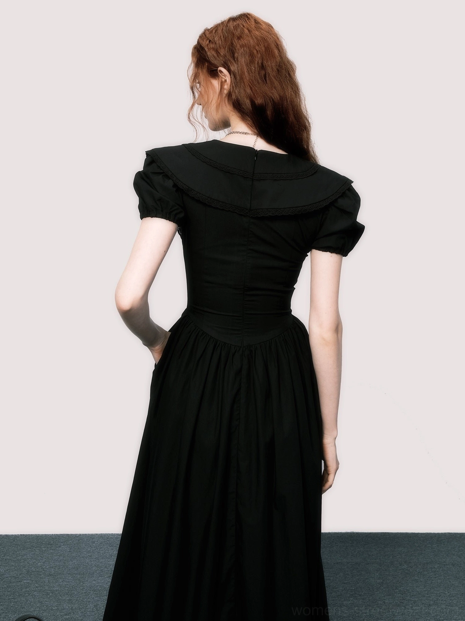 Back view of solid black little black midi dress with puff sleeves, fitted waist, and flowing A-line skirt