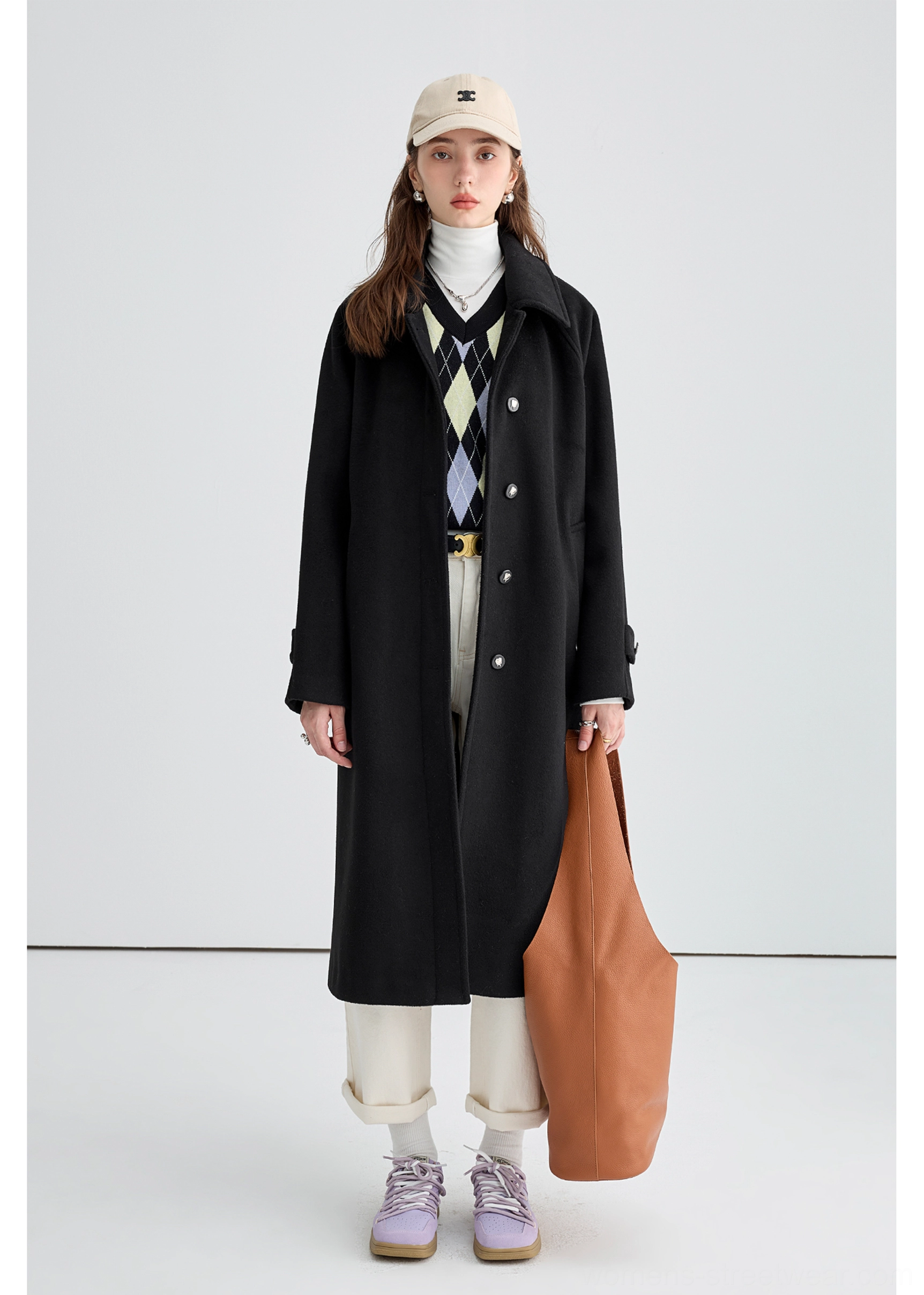 Black long insulated streetwear overcoat styled with white trousers sneakers and a baseball cap for casual city layering