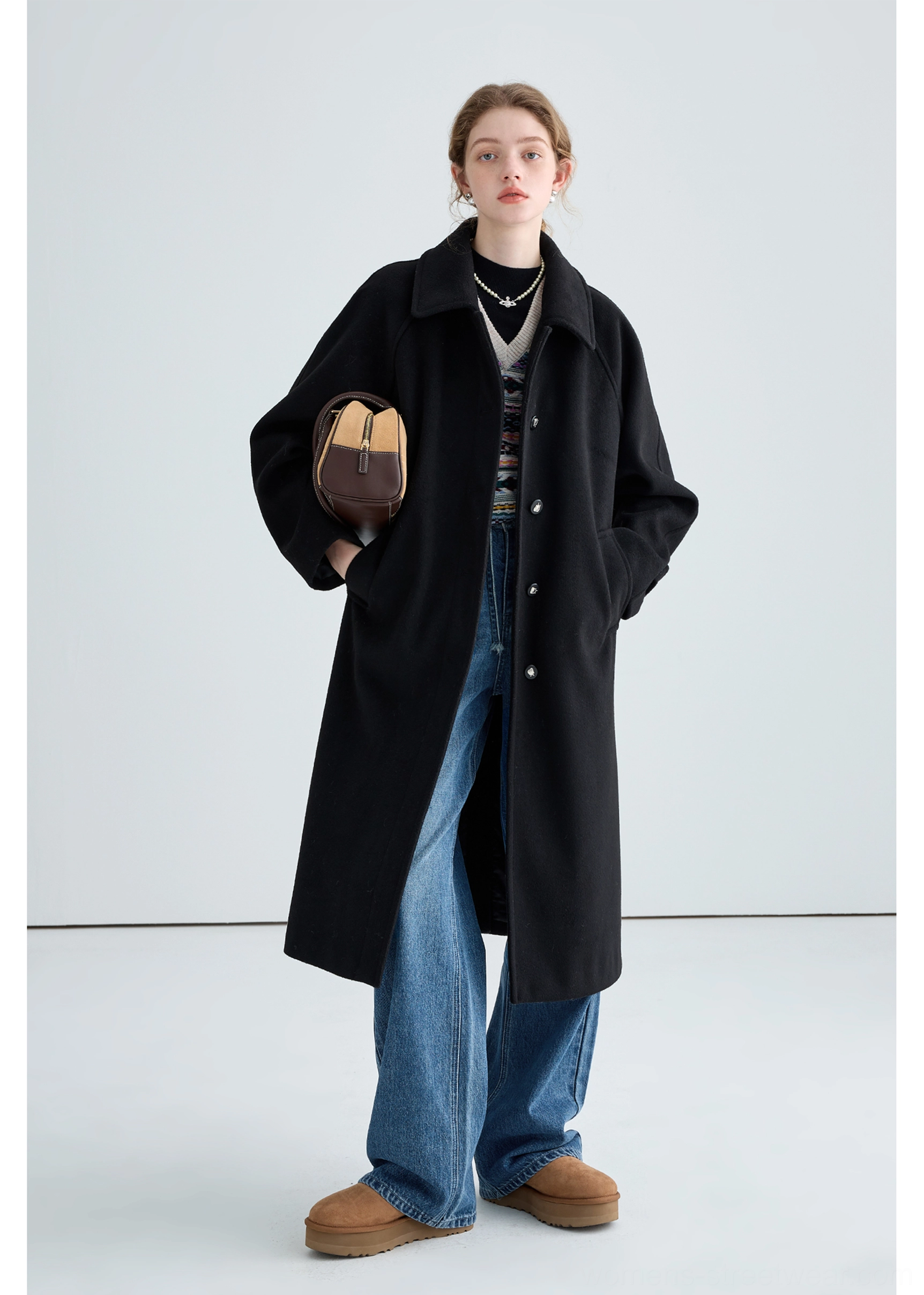 Black long insulated streetwear overcoat styled with wide-leg jeans and shearling loafers in a three-quarter front view