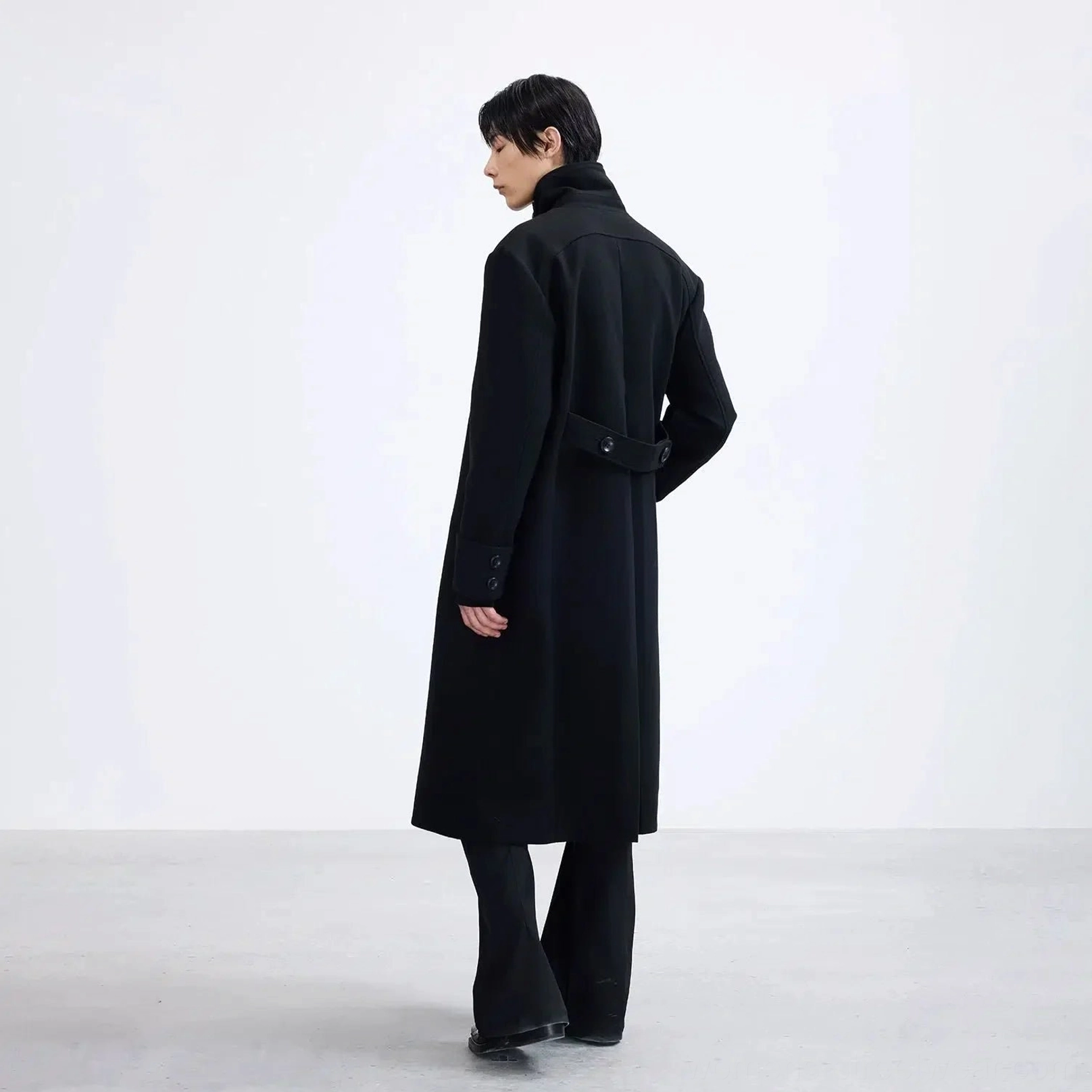 Rear view of a long black polyester overcoat showing the full-length draped silhouette and adjustable back waist detail