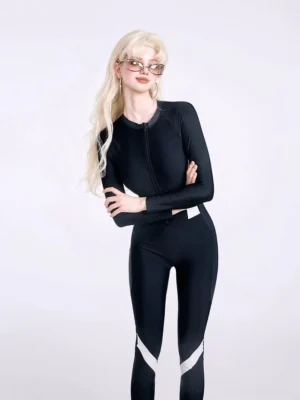 Three quarter front view of black long sleeve one piece swim jumpsuit with fitted silhouette, front zipper, and white lower leg stripe details