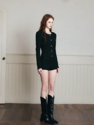 Side full-body view of a woman wearing a black long-sleeve tweed romper with a slim tailored fit, decorative front buttons, cinched waist, and short tailored shorts