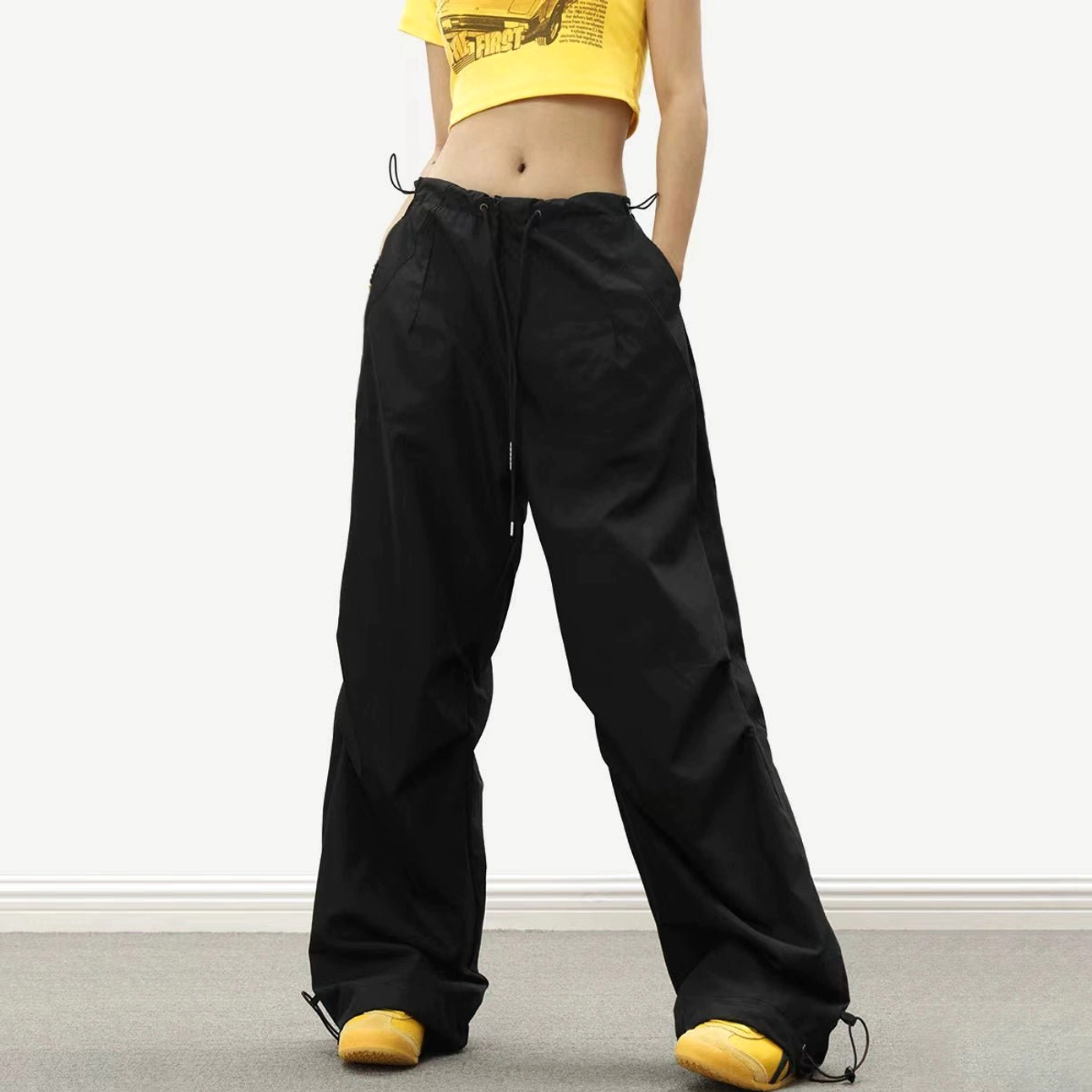 Black loose-fit parachute wide-leg track pants with drawstring waist and adjustable ankle ties styled with a yellow cropped top