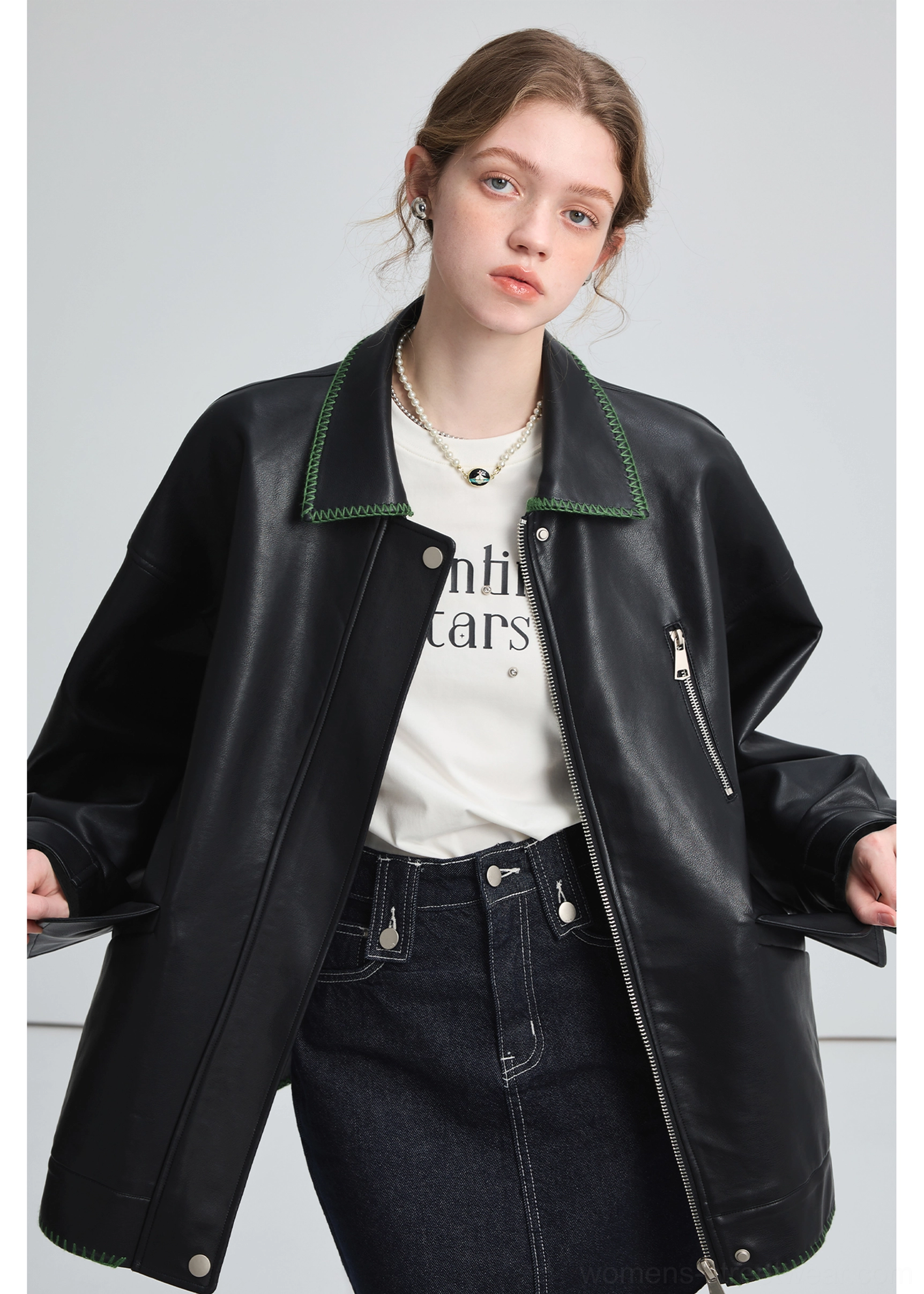 Side front view of a woman wearing a loose black PU leather biker jacket with exposed chest zipper and contrast collar stitching