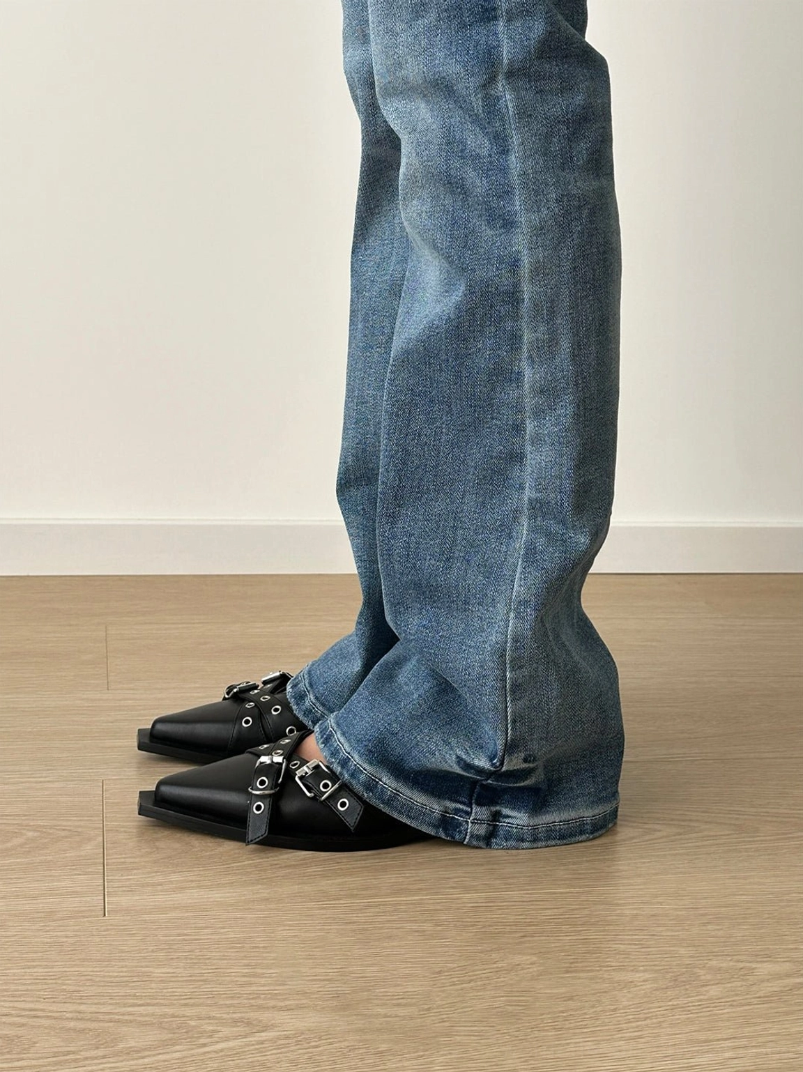Black low-heel buckle Mary Jane flats shown from the side while worn with blue flared denim pants