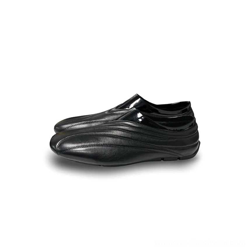 Black low-profile leather slip-on shoes with flowing curved seam details displayed on a clean white studio background