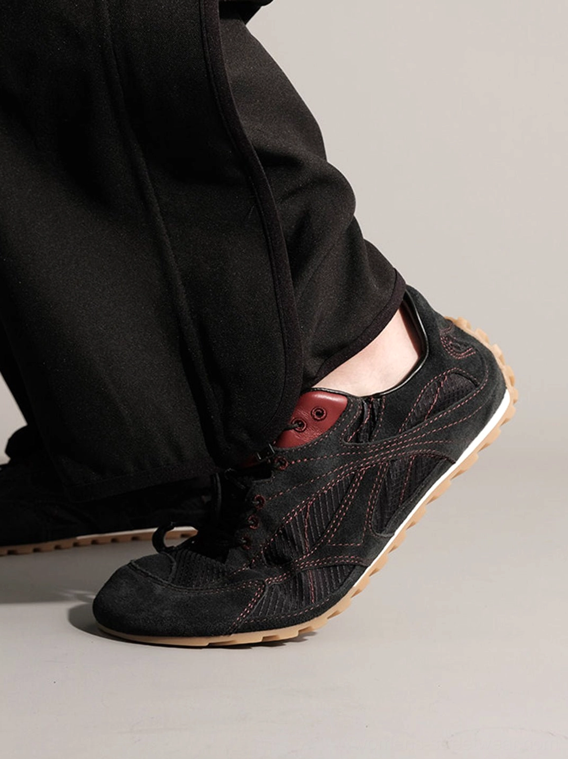 Side profile of black low-top nubuck trainers with contrast stitching and gum sole