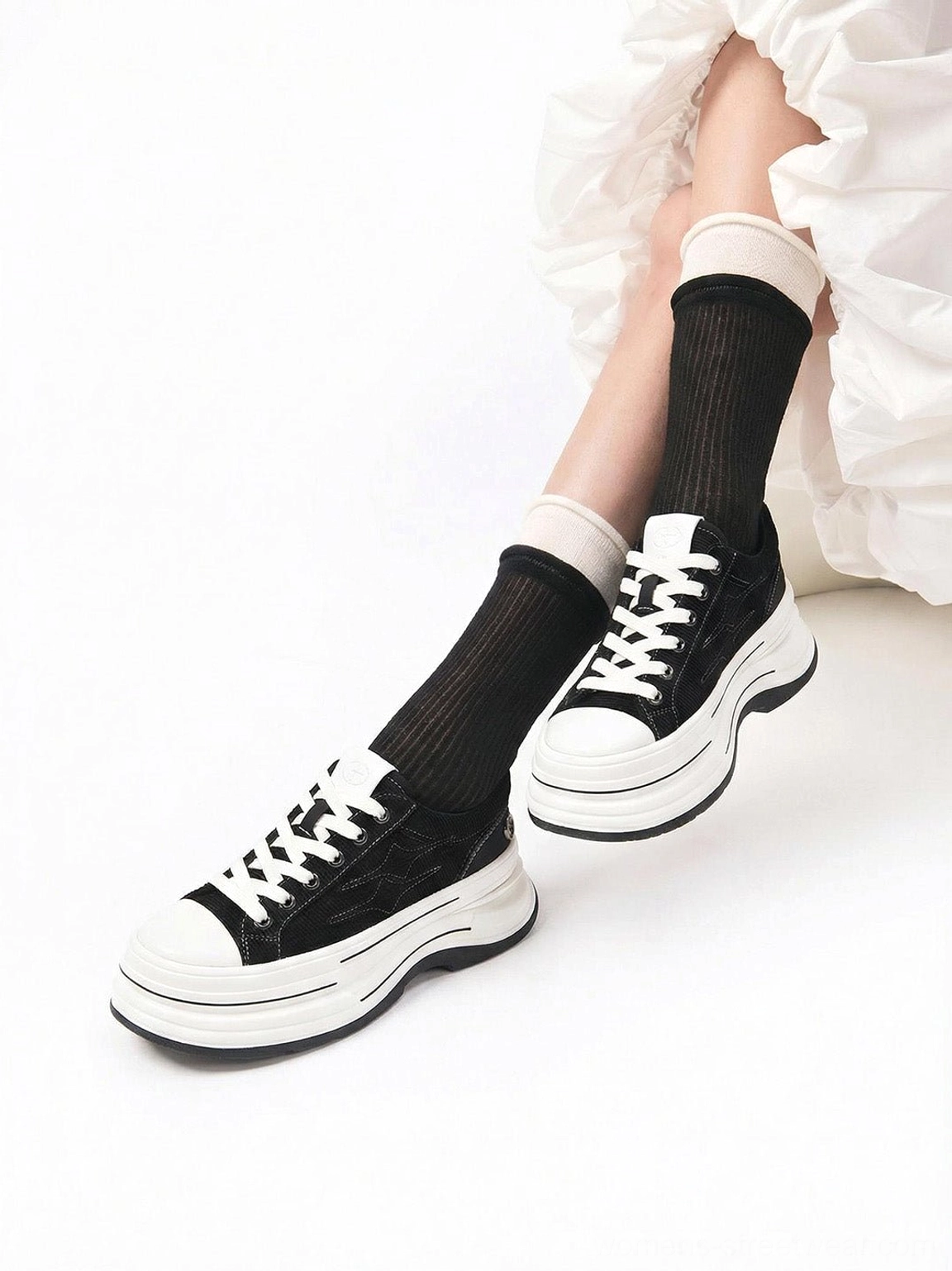 Top-down view of black low-top platform canvas sneakers worn with black crew socks and a white ruffled skirt
