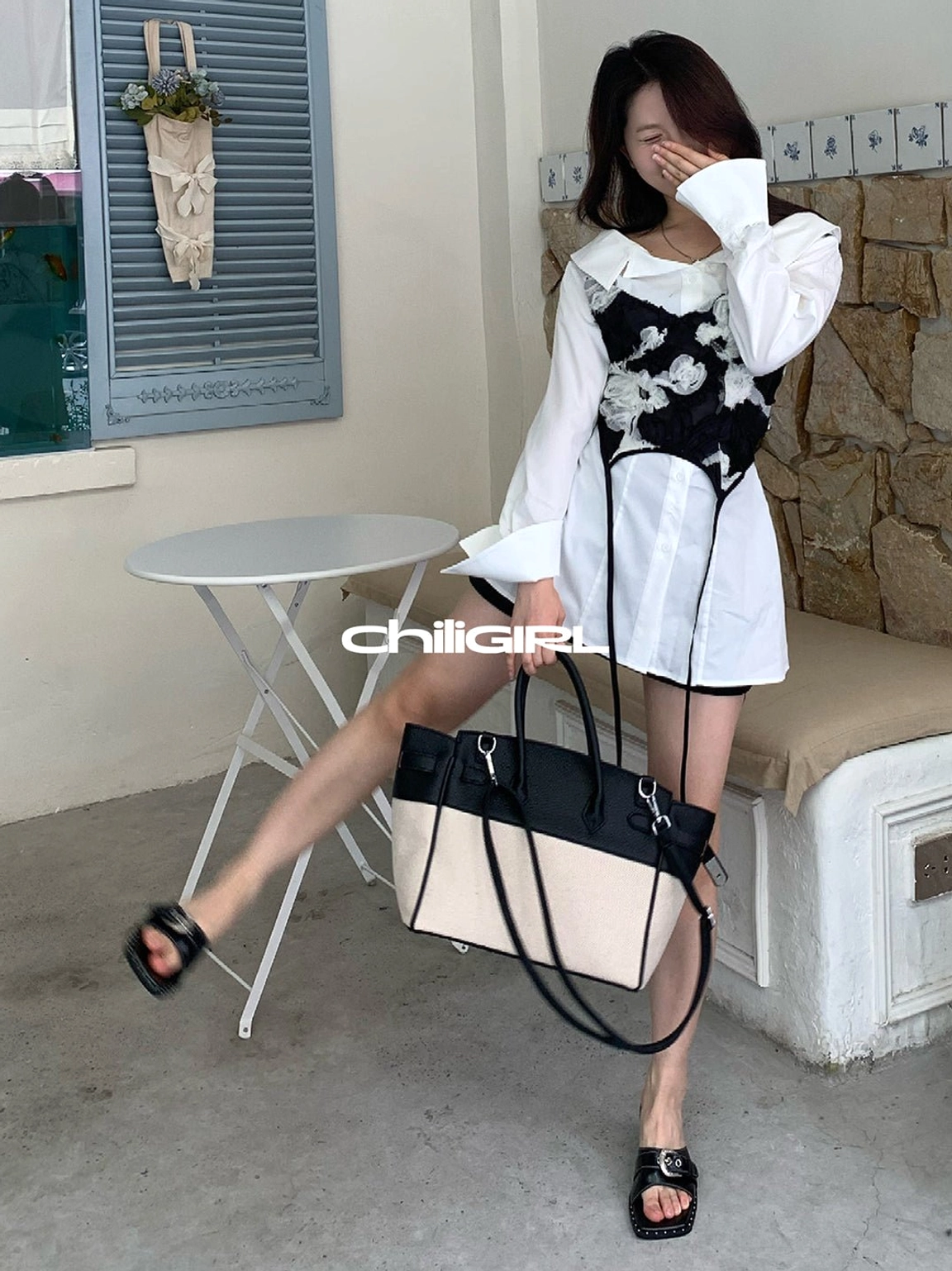 Black low-wedge buckle slide sandals shown in motion with a blouse floral skirt and handbag