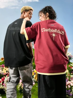Two models wearing oversized embroidered streetwear T-shirts in black and maroon with Gothic back graphics and layered faux two-piece details