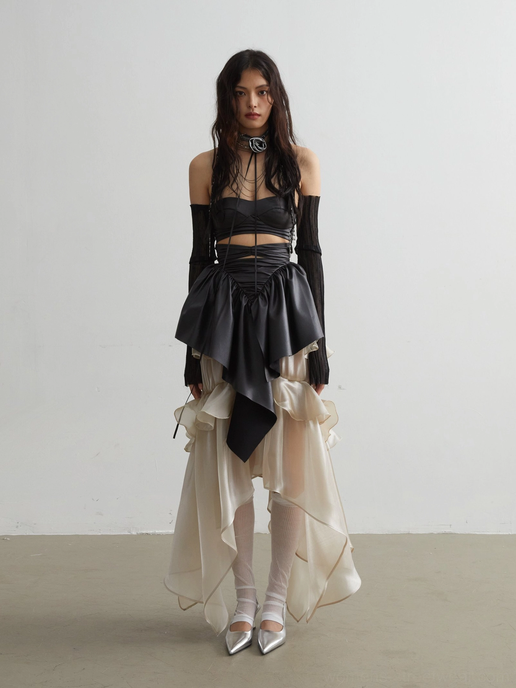 Black ruffled corset crop top styled with a layered sheer midi skirt, silver heels, and white stockings for gothic evening fashion