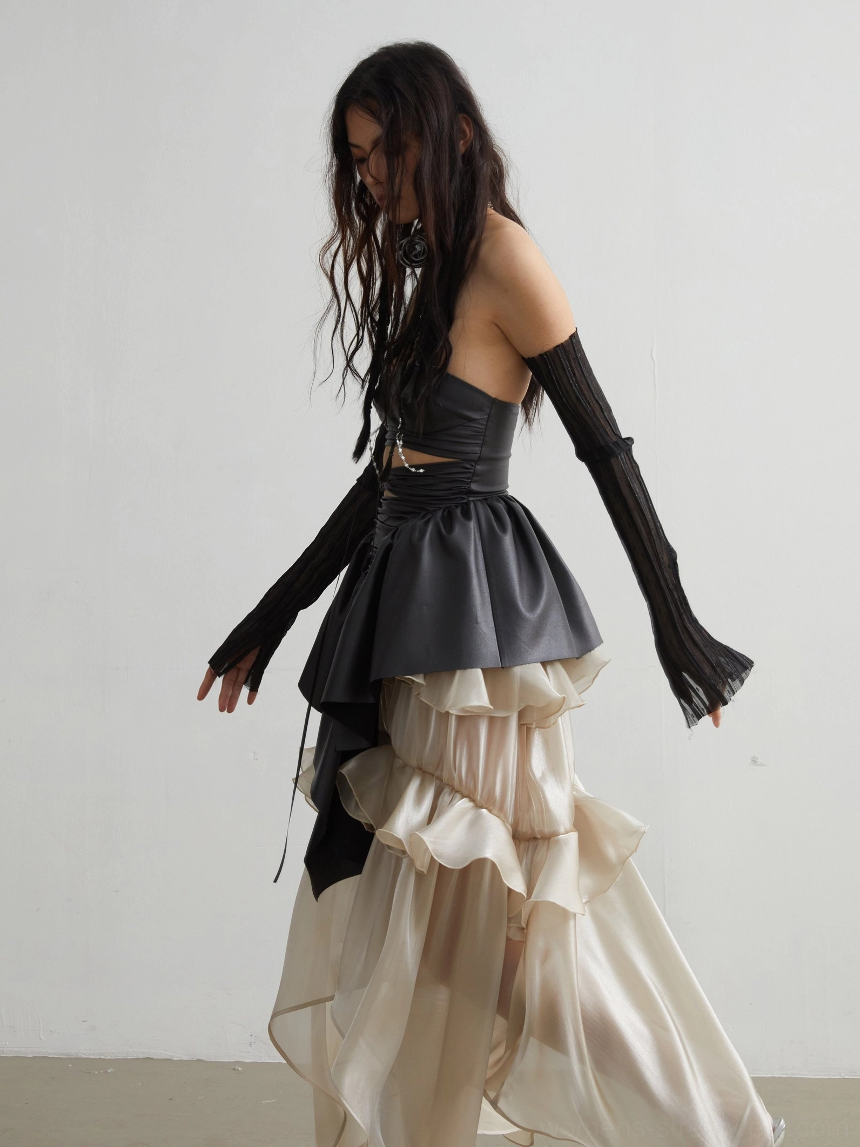 Side profile of black matte PU corset crop top with sculptural asymmetric ruffled peplum for dark romantic streetwear styling
